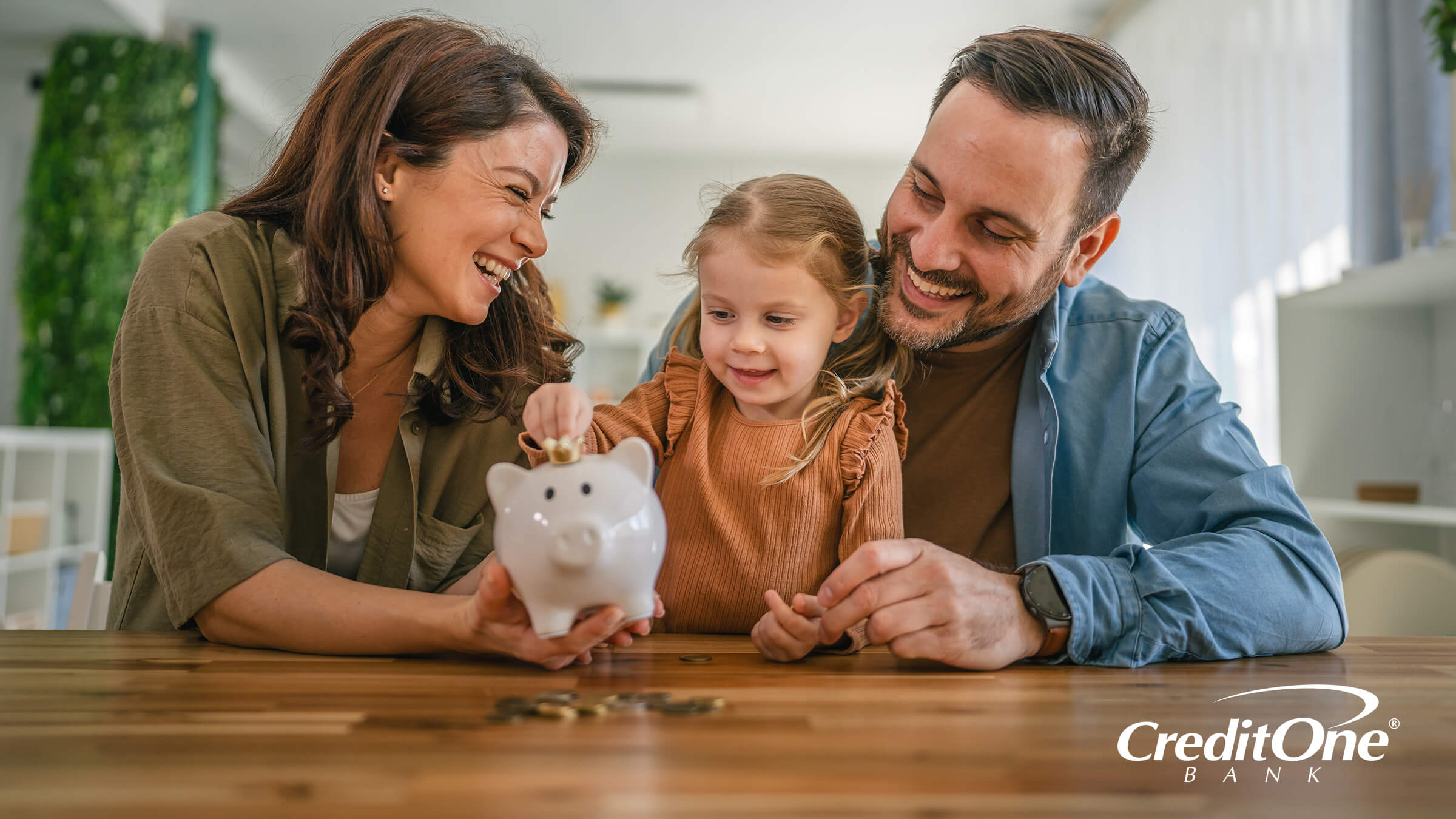 A young girl puts coins in her piggy bank with the help of her parents, who may be teaching her the importance of starting early to build wealth.